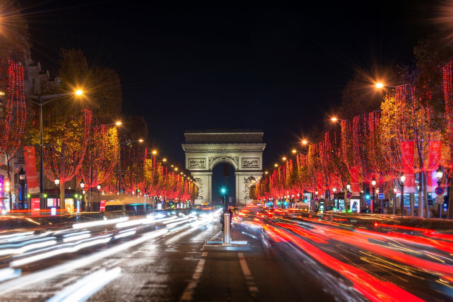 Christmas in Paris: Food, lights and festive activities Champs Elysees avenue and the Arc de Triomphe decorated with red Christmas lights at night in Paris, France.